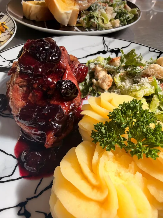 Plato de cerdo con cerezas, puré y ensalada César servido en Casita de Chuao